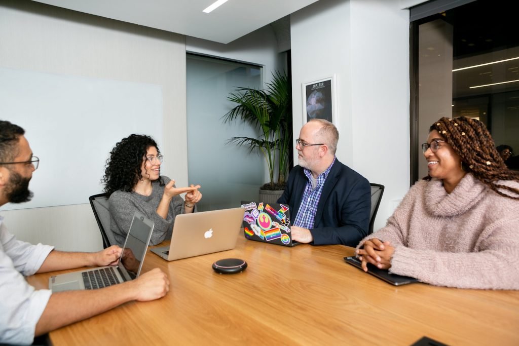 A diverse group of four coworkers chatting in a meeting room.