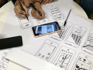 People drawing on paper with drawings of phone screens and a phone on the table